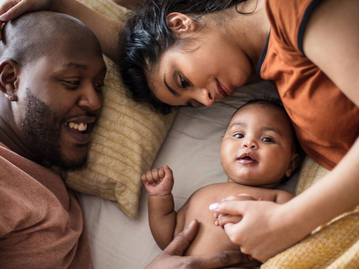 A man and woman lying on a bed, cuddling with a baby.