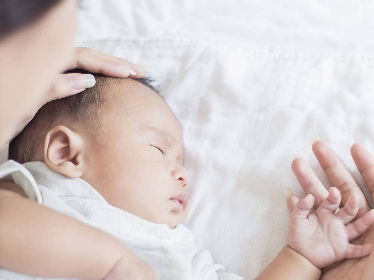 A woman gently caressing an infant who is lying on a white sheet.