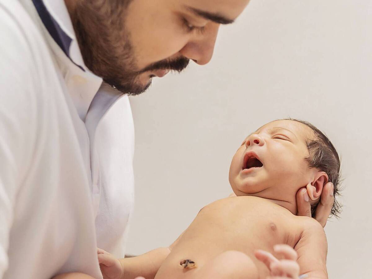 A man gently holding a newborn, cradling their head and body. 