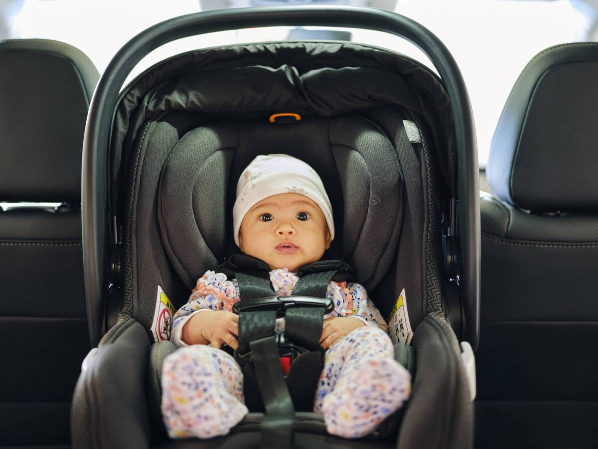 A young baby safely sitting in a car seat, facing the back of a vehicle.