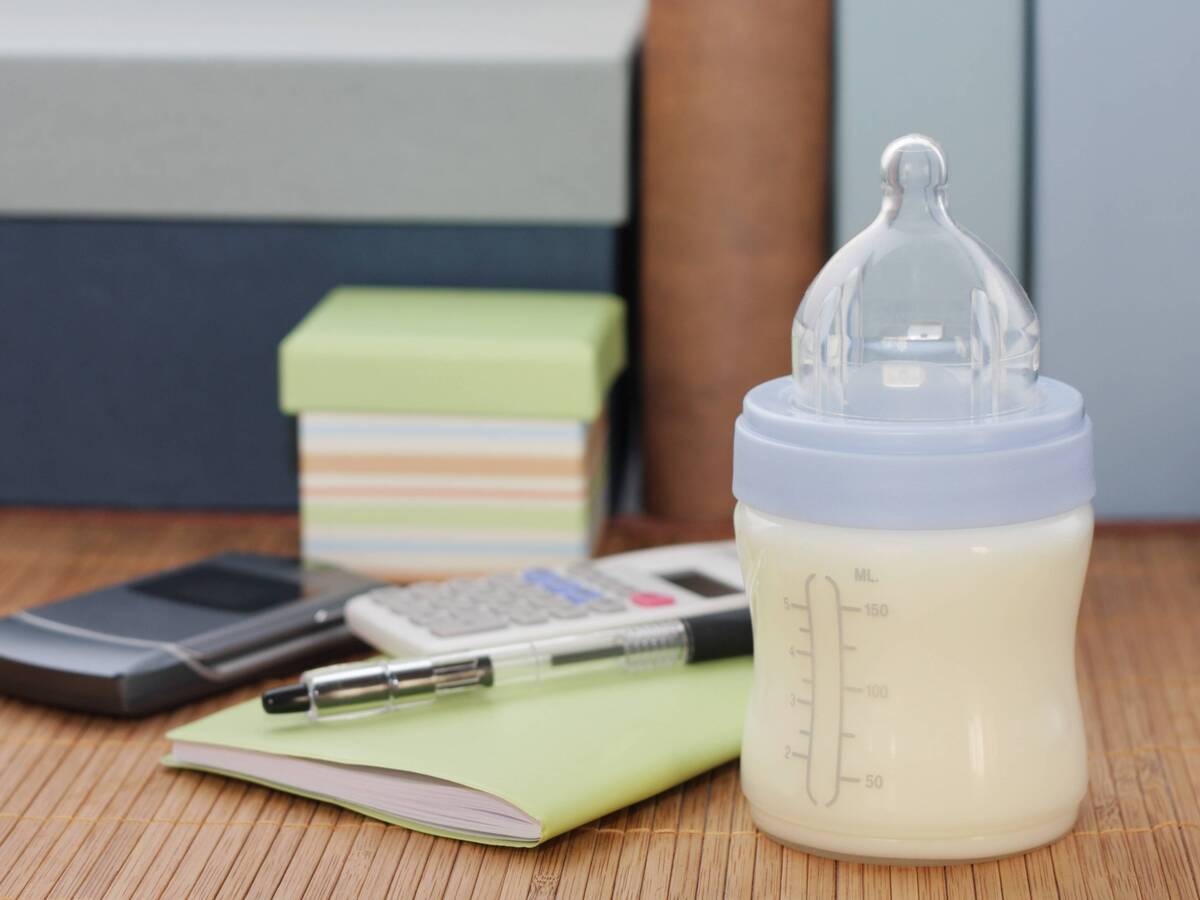 A desk with small bottle of breastmilk, pen, notebook, calculator and cell phone.
