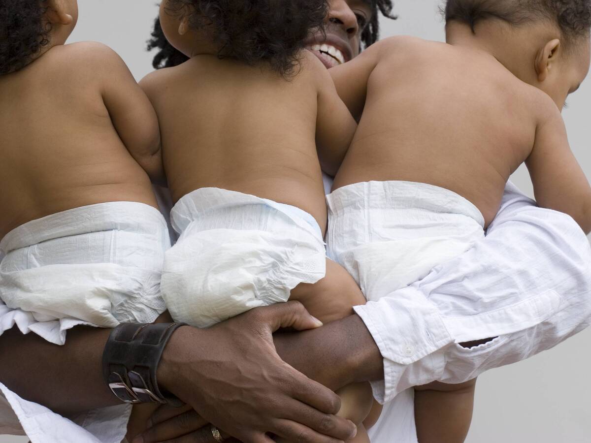 A man holding triplet babies in diapers in his arms.