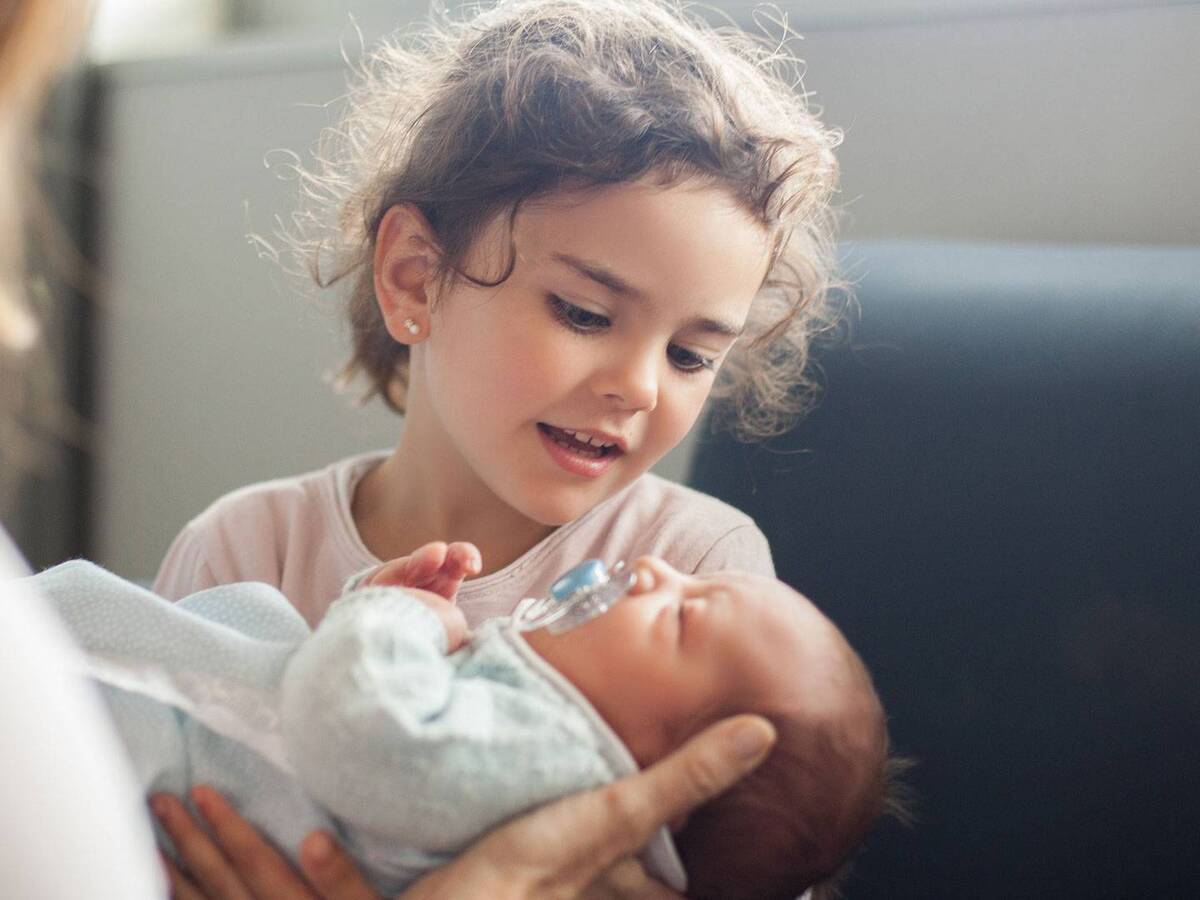 A child gazing down at an infant being held by an adult.