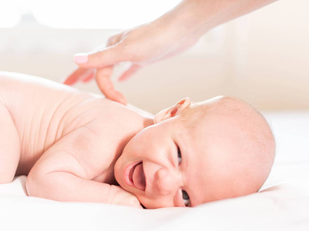 A baby smiling and lying on their tummy, while someone gently strokes their back.