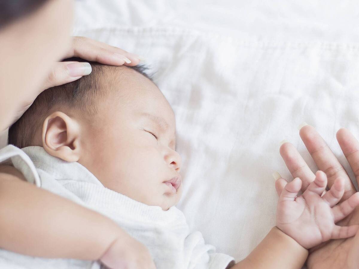 A woman gently caressing an infant who is lying on a white sheet.