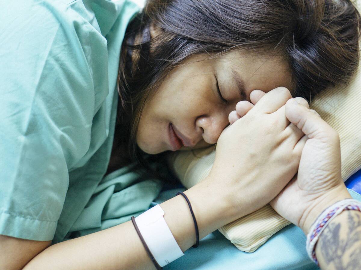 A woman wearing a hospital ID bracelet and holding someone's hand for comfort.