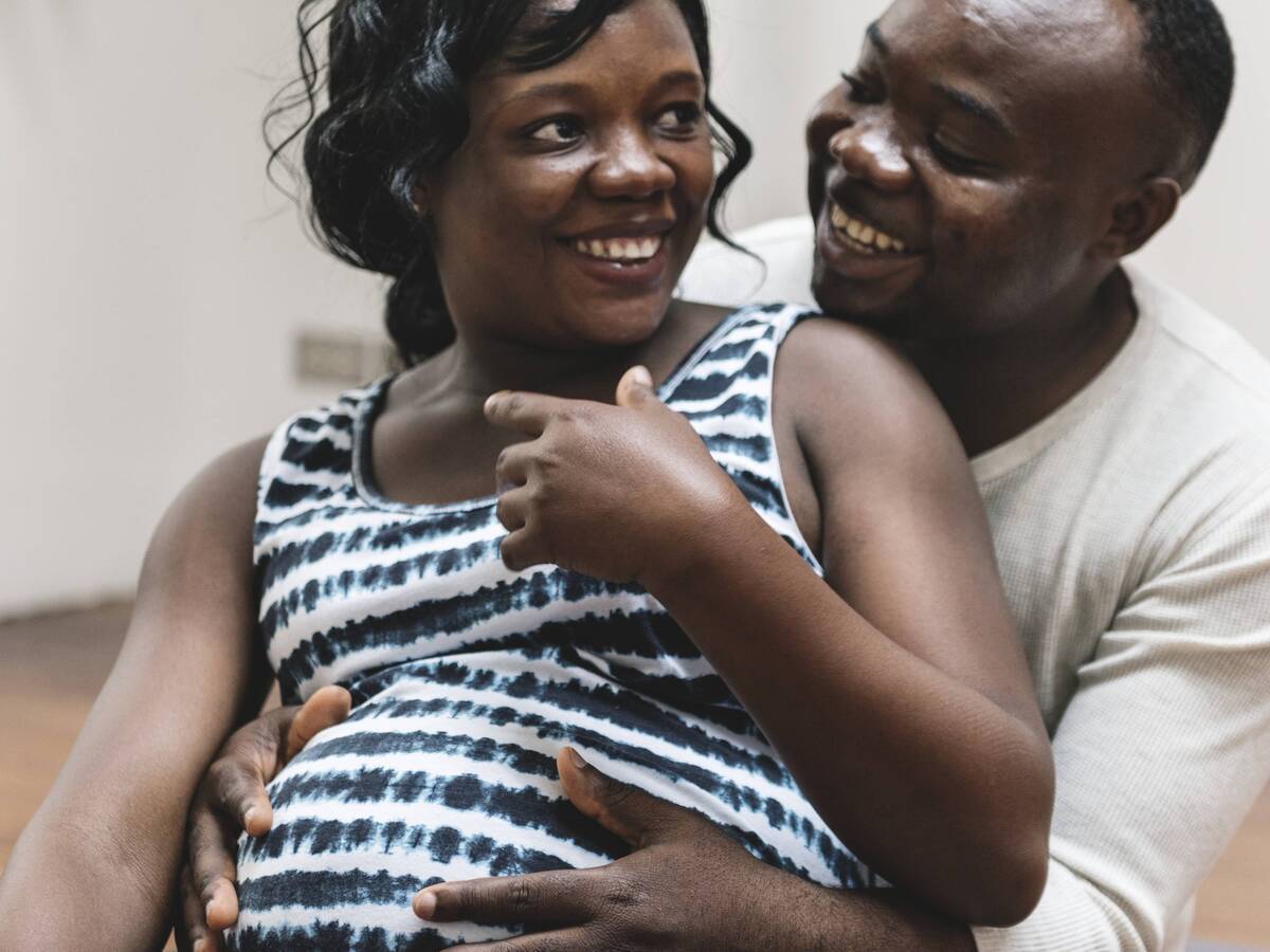 A pregnant woman smiling at her partner over her shoulder, while he holds her belly.