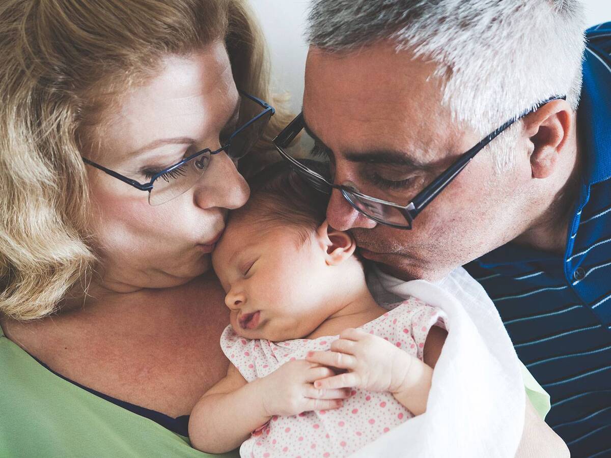 An older woman and man gently kissing the top of an infant's head.