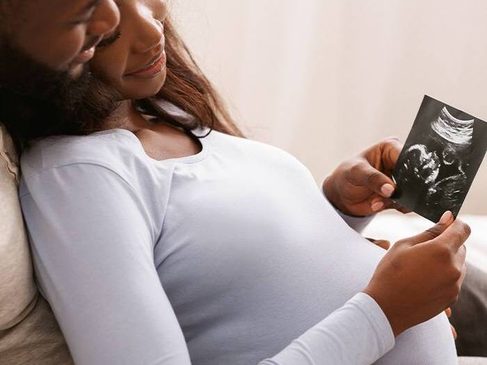 A pregnant woman holding an ultrasound picture while she leans back into her partner. 