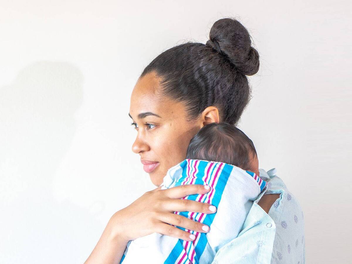 A woman cradling a swaddled infant on her shoulder.