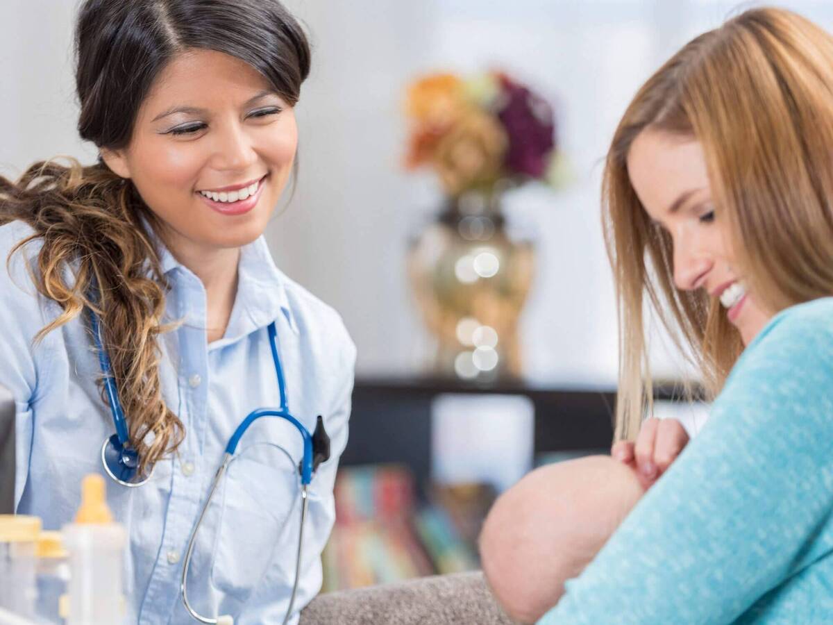 A woman feeding an infant while a medical professional observes.